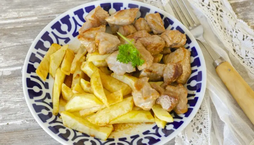 Un plato de raxo con patatas fritas, decorado con perejil fresco. Un clásico delicioso.