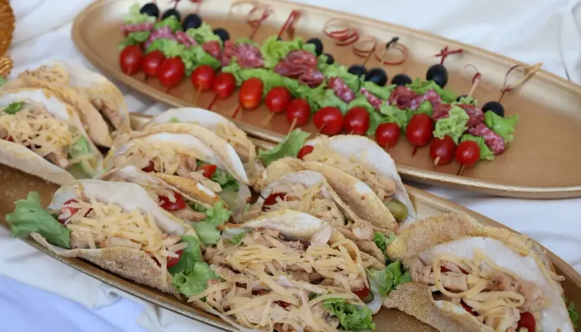 Un buffet froid mariage avec des tacos garnis de poulet, salade et fromage râpé, et des brochettes de tomates, olives et salami.