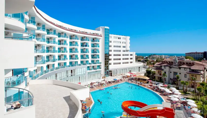 Hotel Narsia Resort: biały, nowoczesny budynek z niebieskimi balkonami i basenem z atrakcjami wodnymi. Słoneczny dzień, wakacyjna atmosfera.