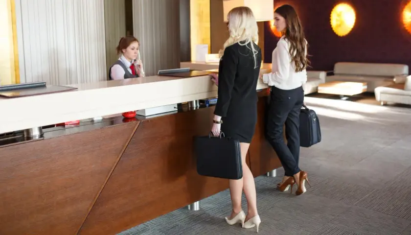 La receptionist accoglie i clienti che arrivano in albergo. Due donne d'affari con valigette attendono al bancone.