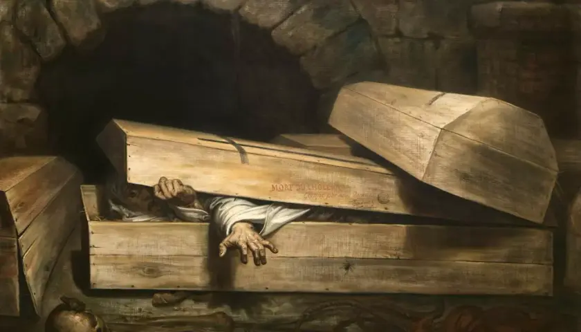 Człowiek próbuje wydostać się z trumny, budząc grozę tafefobii. Obok czaszka i kości.