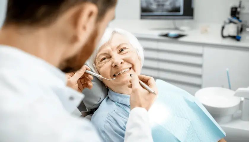 Un dentista esamina i denti di un'anziana sorridente, sottolineando l'importanza dell'igiene orale per gli anziani.