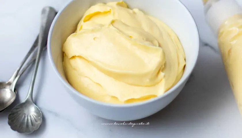 Crema pasticcera con panna, soffice e vellutata, pronta per farcire dolci. Accanto, cucchiaini d'argento e sac à poche.