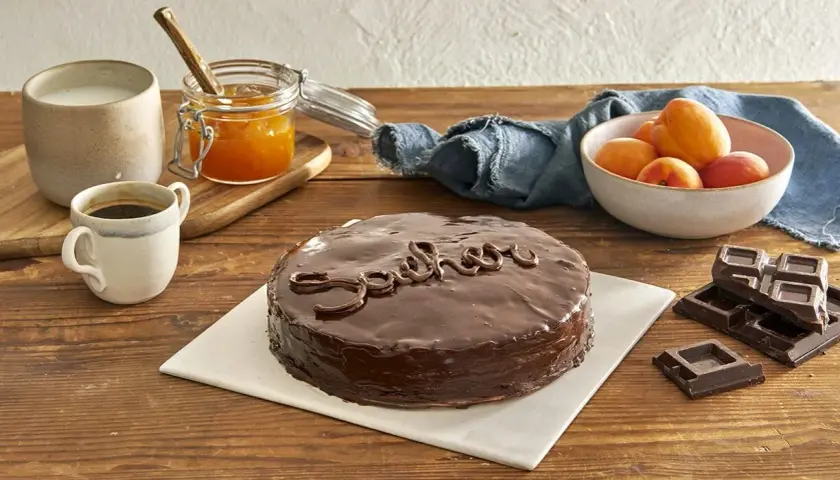 Una deliziosa torta Sacher, lucida e ricoperta di cioccolato, pronta per essere gustata con caffè, albicocche e cioccolato fondente.