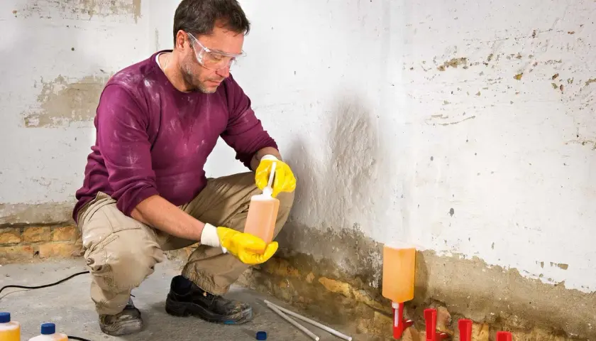 Mann mit Schutzbrille und Handschuhen behandelt feuchte Wand mit Injektionsflüssigkeit. So wird die Wand trocken.