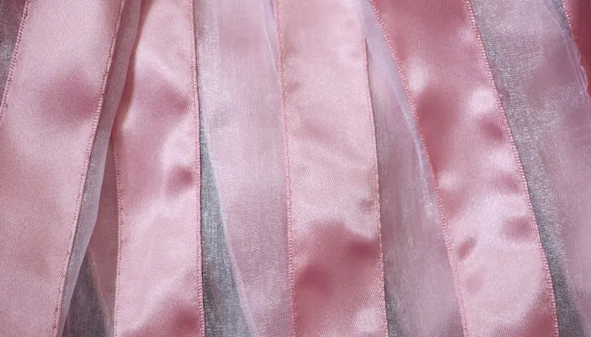 Bandes verticales de tissu brillant rose et argenté, créant un effet de texture doux et lumineux.