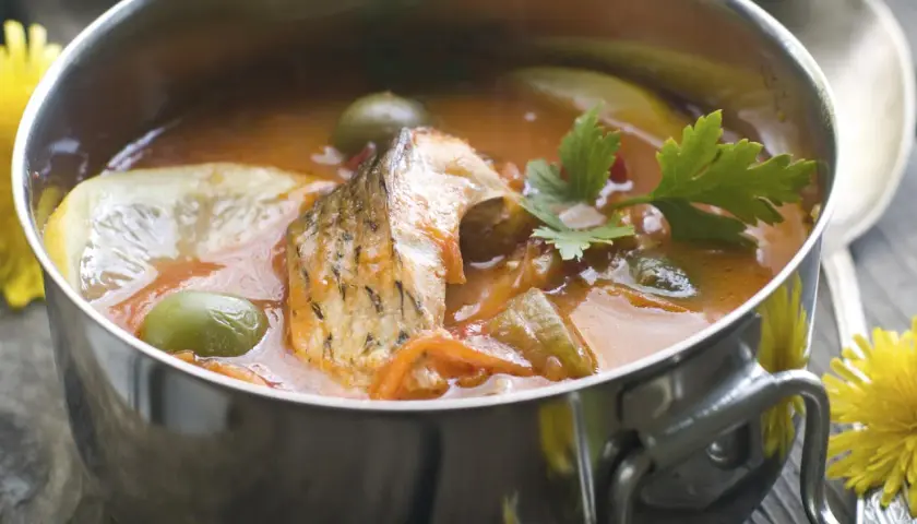 Aromaticzna rosyjska zupa rybna z kawałkami ryby, oliwkami, cytryną i natką pietruszki w metalowej misce.