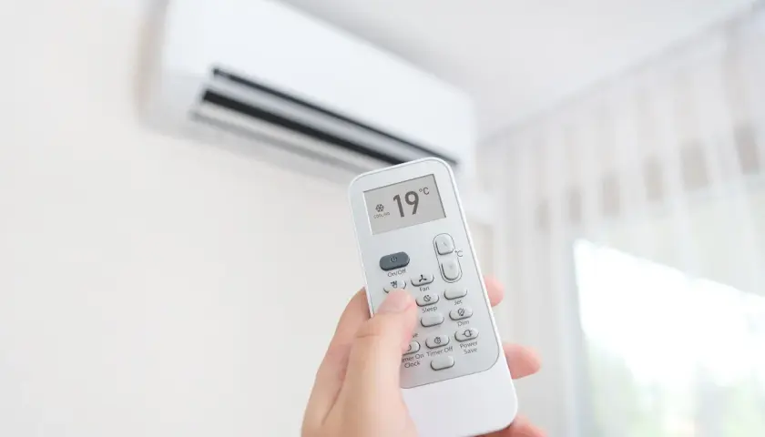 Mano sujetando control remoto de aire acondicionado, ajustando el símbolo frío a 19°C para un ambiente fresco.