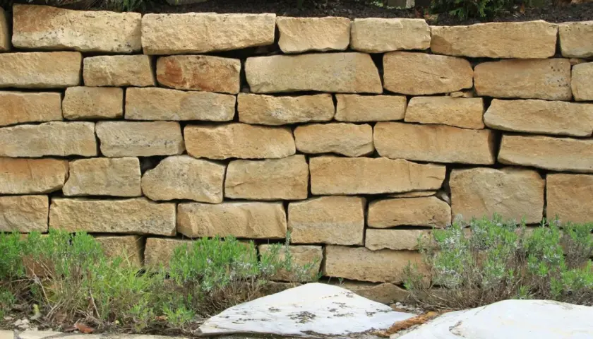 Eine rustikale Natursteinmauer bauen, die mit Lavendel und Steinen verziert ist.