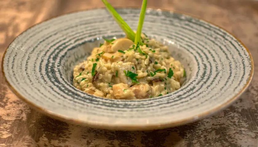 Kremowe risotto ze szparagami i grzybami, udekorowane zieloną cebulką i natką pietruszki, podane w ozdobnej misce.