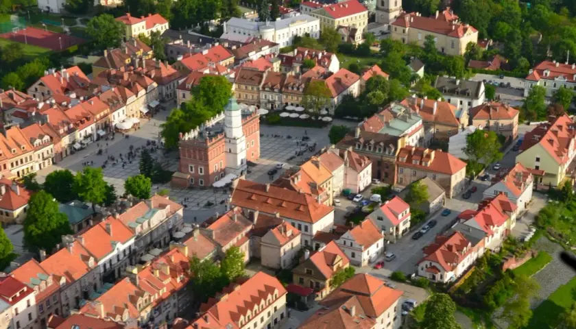 Urokliwe zabytkowe miasto nad Wisłą, z Rynkiem i wieżą ratuszową, otoczone kamienicami z czerwonymi dachami.