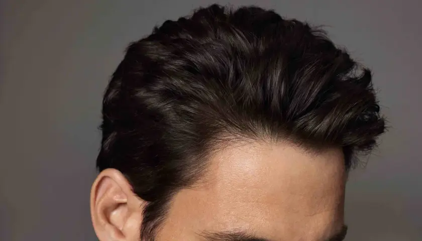Primer plano de un hombre con mas cantidad de pelo oscuro y peinado hacia atrás, mostrando su oreja y parte de su rostro.