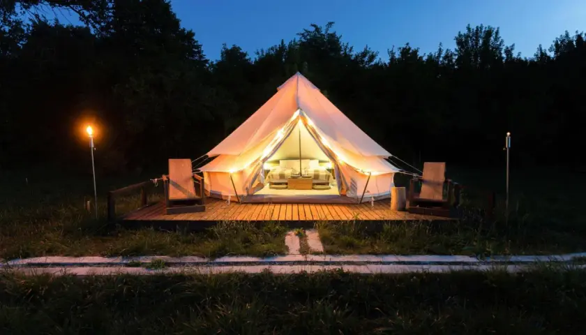Tienda iluminada para camping Portugal, ideal para familias con niños. Dos sillas de madera esperan en la terraza.