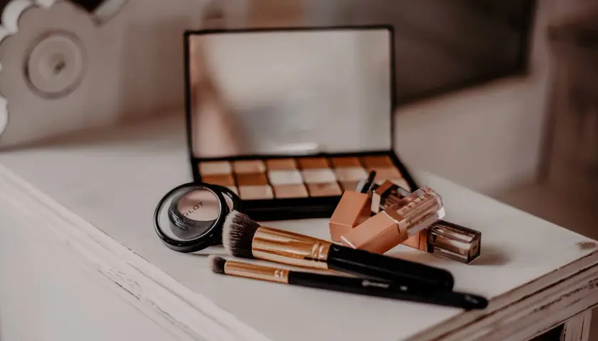 Make-up-Pinsel, Lidschattenpalette, Lippenstifte und Puder auf einer weißen Kommode.