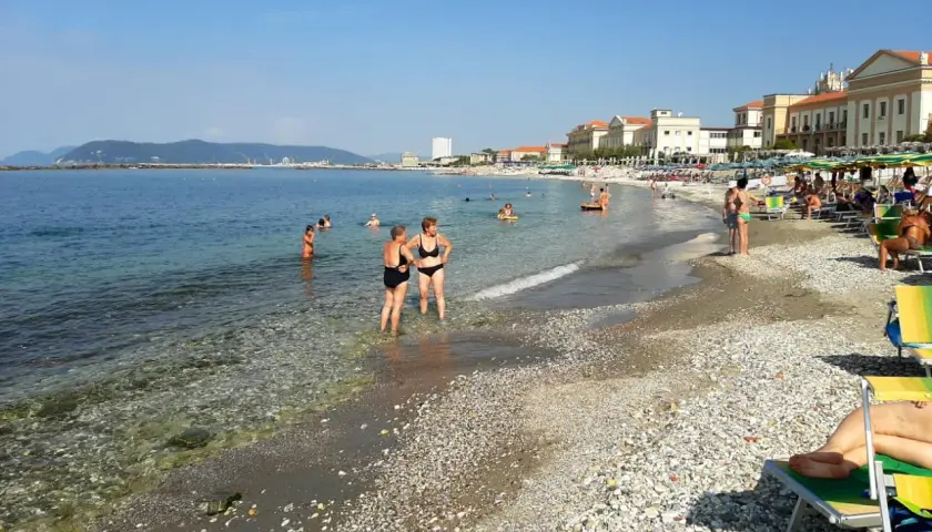 Plage de Massa, Italie. Des baigneurs profitent de l'eau claire et du soleil sur cette plage de galets animée.
