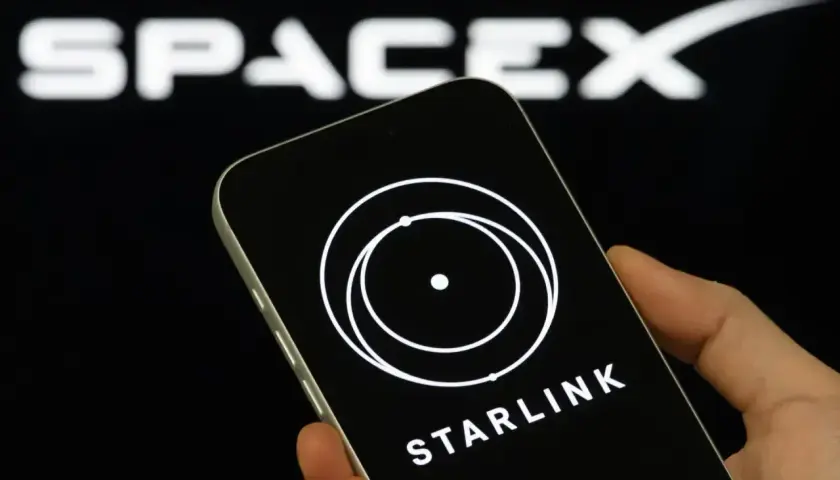 Dłoń trzyma smartfon z logo Starlink na ekranie, w tle logo SpaceX.