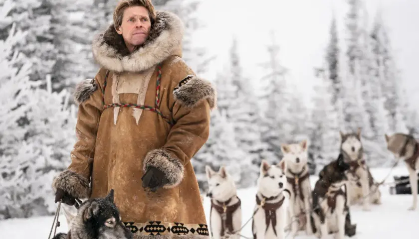 Man i pälsrock med hundspann i snöig skog. Scen från en togo film.