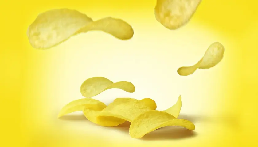 Chrupkie chipsy unoszą się na żółtym tle. Zastanawiasz się, ile kalorii mają chipsy?