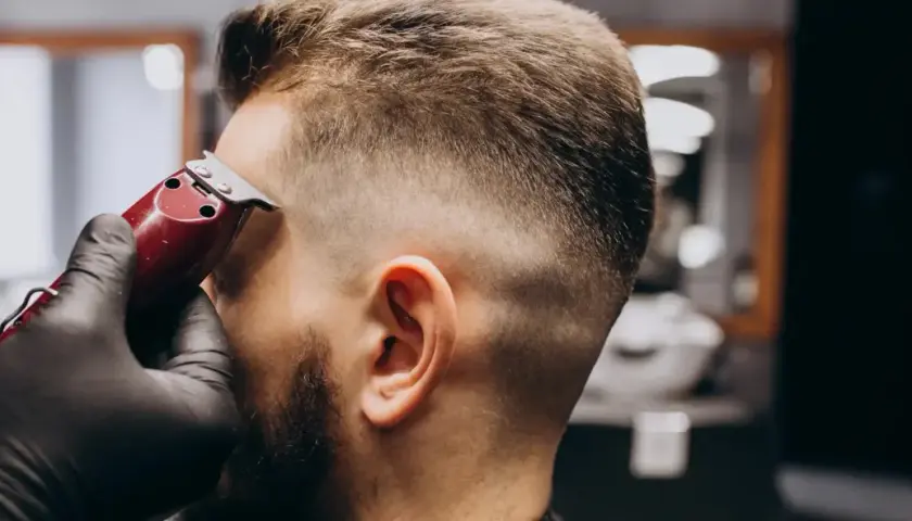 Barbero con guantes negros crea un corte de pelo **low fade** a un hombre con una máquina.