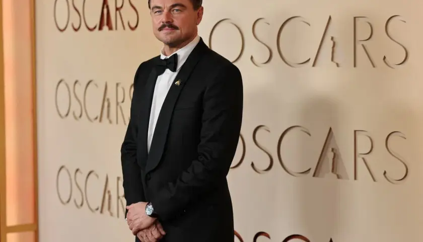 Leonardo DiCaprio w eleganckim smokingu pozuje na tle ścianki z napisem "OSCARS".