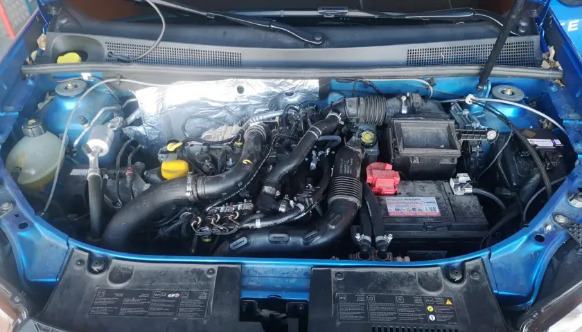 Motor de Dacia Sandero GLP con mangueras de gas y batería. Posibles problemas de instalación o mantenimiento.