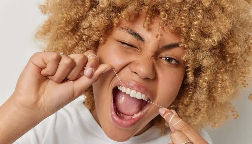 Donna con capelli ricci usa il filo interdentale per una pulizia perfetta.