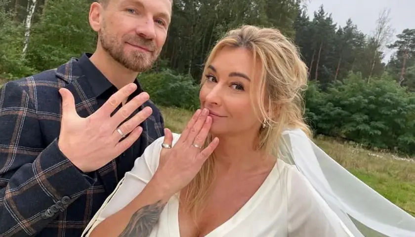 Martyna Wojciechowska i Kossakowski pokazują obrączki. Uśmiechnięci, w plenerze, świętują ważny moment.
