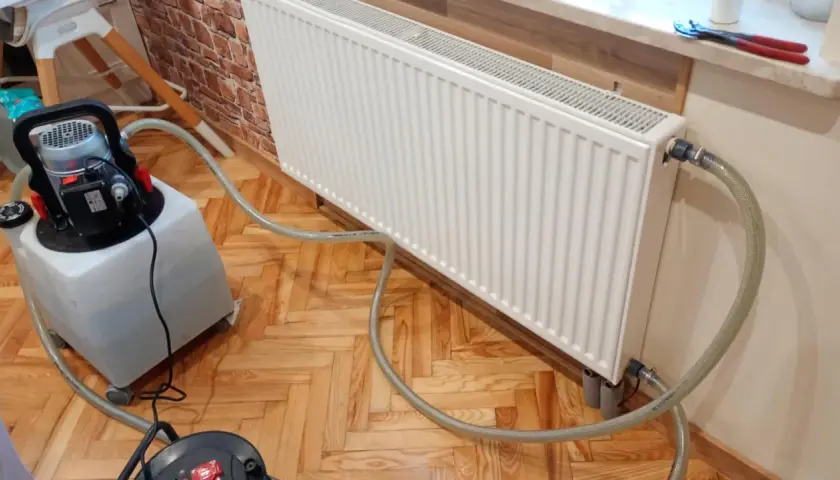 Profesjonalne płukanie instalacji grzewczej w Warszawie. Sprzęt do czyszczenia podłączony do grzejnika.