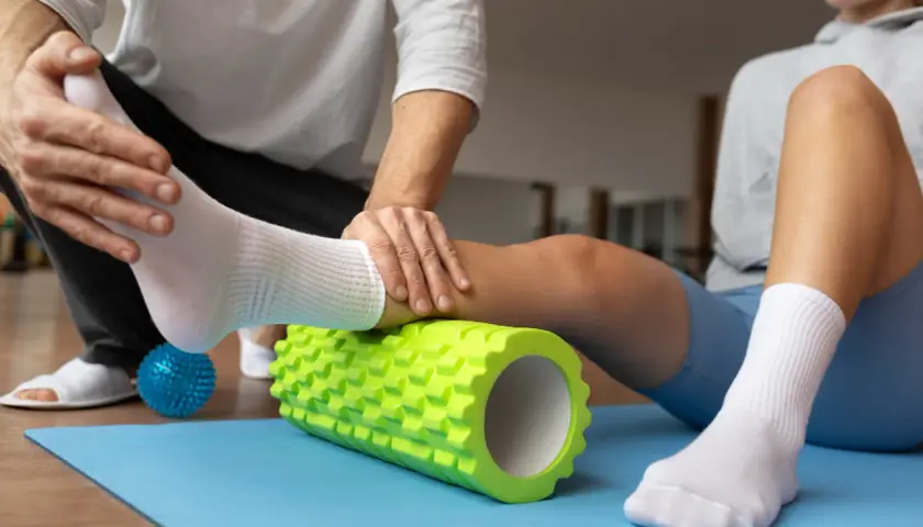 Fizjoterapeuta pomaga sportowcowi w automasażu łydki wałkiem, co jest kluczowe w klinicznej medycynie sportowej.