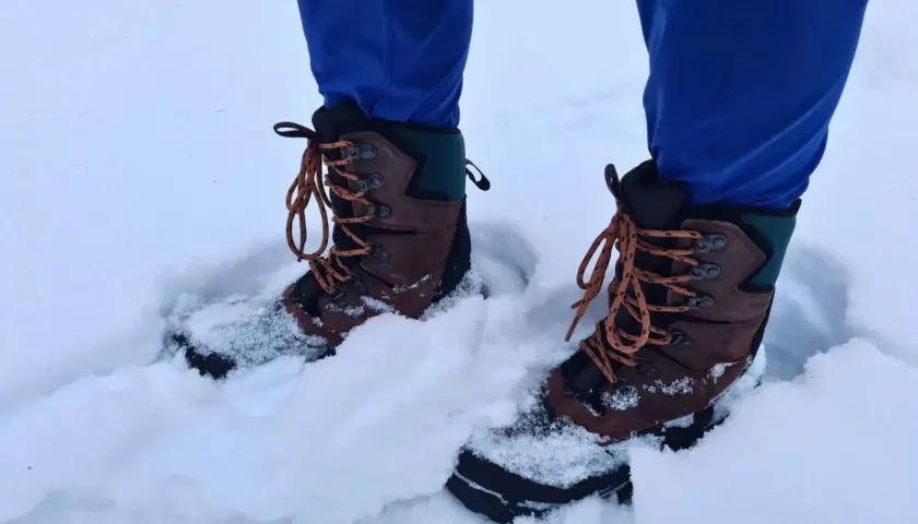 A person wearing blue pants and brown hiking boots stands in deep snow. These boots seem to be performing well, raising the question: can hiking boots be used as snow boots?