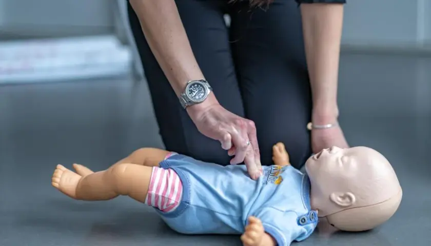 Ćwiczenie reanimacji a resuscytacji niemowlaka na fantomie. Dłoń instruktora uciska klatkę piersiową.