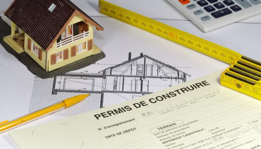 Maquette de maison, plans, mètre, calculatrice et formulaire "Permis de construire". La question : peut-on commencer les travaux pendant le recours des tiers ?
