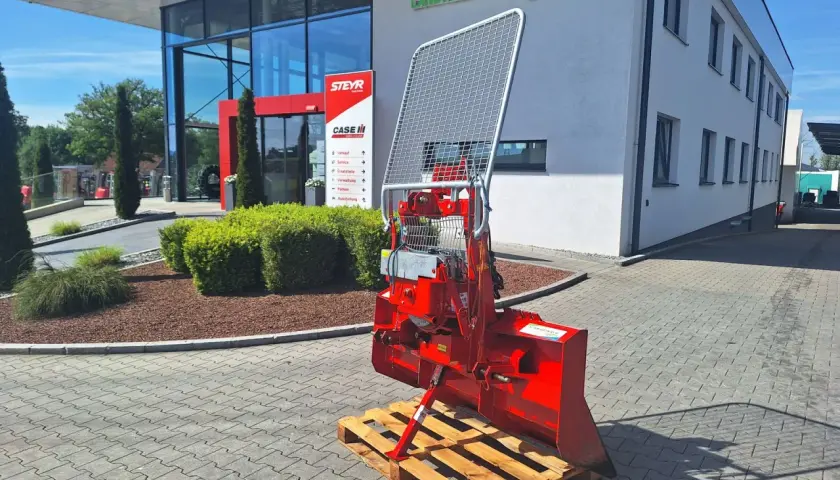 Roter Forstkran auf einer Palette vor einem Landtechnik-Gebäude. Ein robustes Gerät für den Einsatz im Wald, bereit für den Transport.