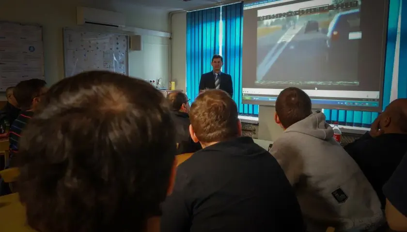 Uczestnicy kursu reedukacyjnego oglądają film z jazdy samochodem na ekranie.