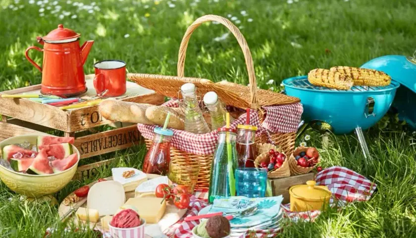 Idealne jedzenie na piknik: kosz pełen smakołyków, grillowana kukurydza, sery, owoce i napoje.