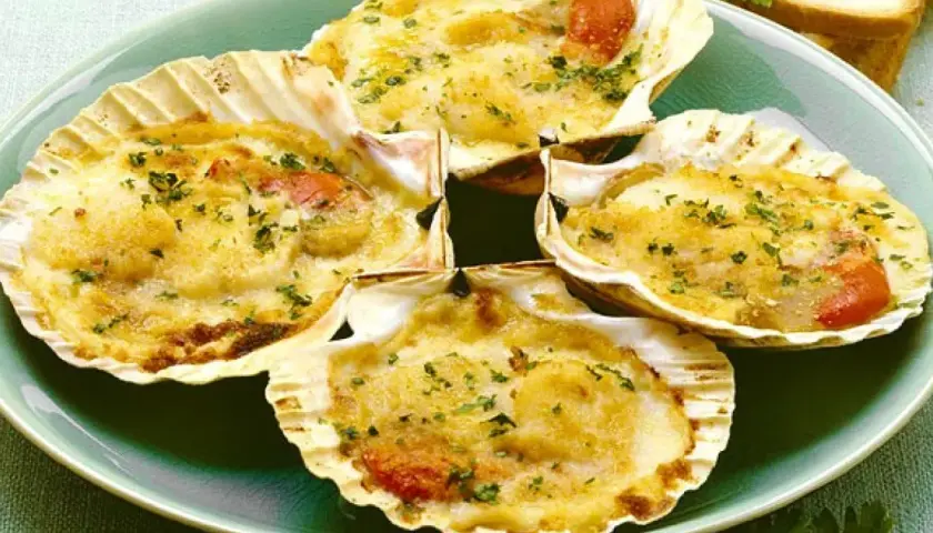 Quattro capesante gratinate, un delizioso antipasto di pesce, servite in conchiglia con erbe aromatiche.
