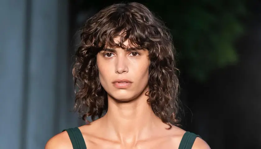 Mujer con pelo rizado con flequillo, mirada intensa y vestido verde oscuro.