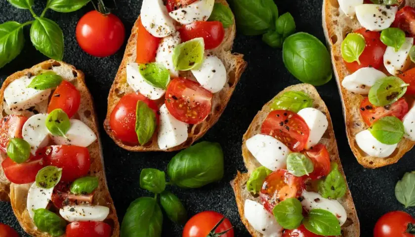 Chrupiące grzanki z pomidorami i mozzarellą, ozdobione świeżą bazylią. Idealna przekąska na lato.