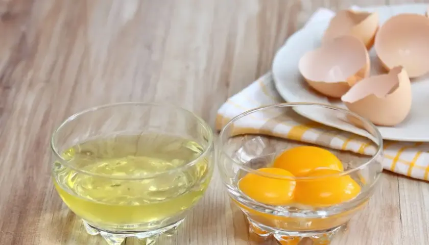 Deux bols en verre sur une table en bois : l'un contient du blanc d'œuf, l'autre des jaunes. Des coquilles d'œufs vides sont sur une assiette. Idéal pour la conservation du blanc d'œuf.
