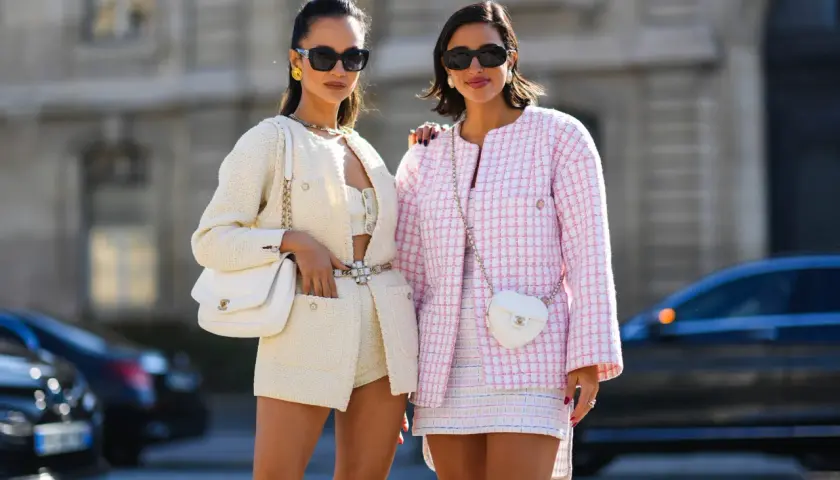 Dos mujeres lucen conjuntos de tweed, uno blanco y otro rosa, encarnando la moda preppy con bolsos a juego y gafas de sol.
