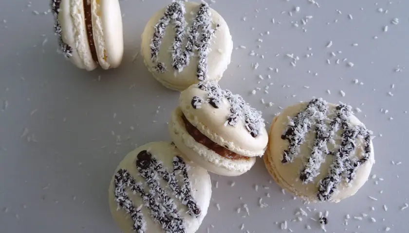 Macarons à la ganache coco, parsemés de noix de coco râpée et de copeaux de chocolat noir.
