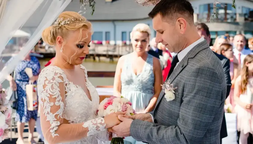 Para młoda wymienia obrączki podczas ceremonii ślubu konkordatowego. Dokumenty ślubne czekają na podpisanie.