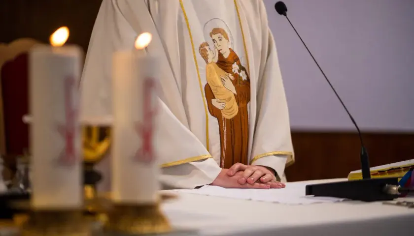 Szczegół szaty kapłańskiej z haftem świętego z dzieckiem, świece i mikrofon.