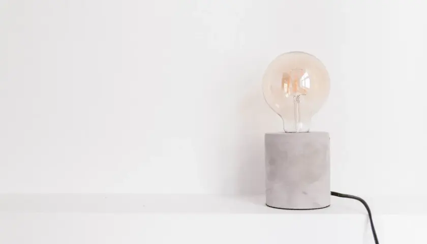 Bombilla Edison de cristal transparente sobre base de cemento gris con cable negro.
