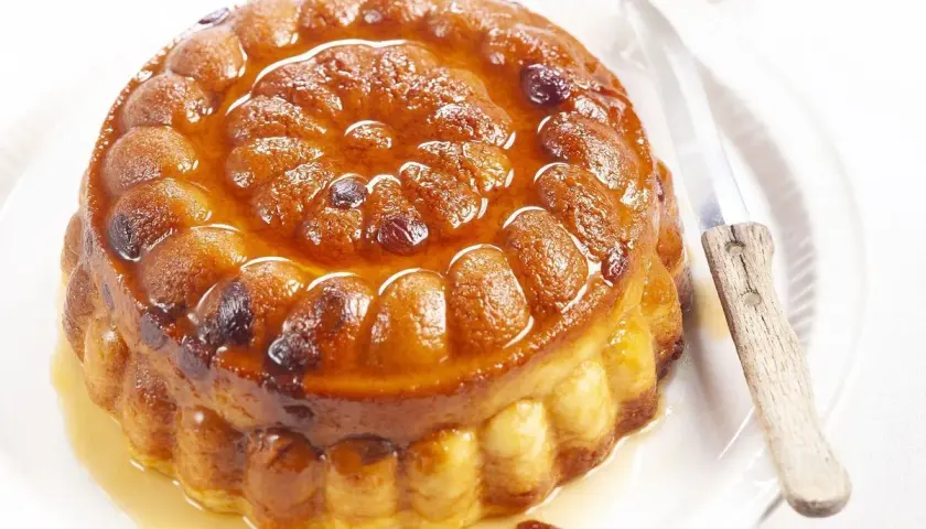Gâteau de semoule doré et moelleux, nappé d'un sirop ambré et parsemé de raisins secs. Un couteau est posé à côté, prêt à découper cette gourmandise.