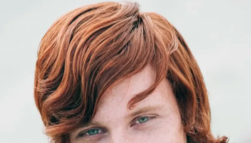 Ojos verdes y cabello pelirrojo ondulado, con pecas visibles en la piel.