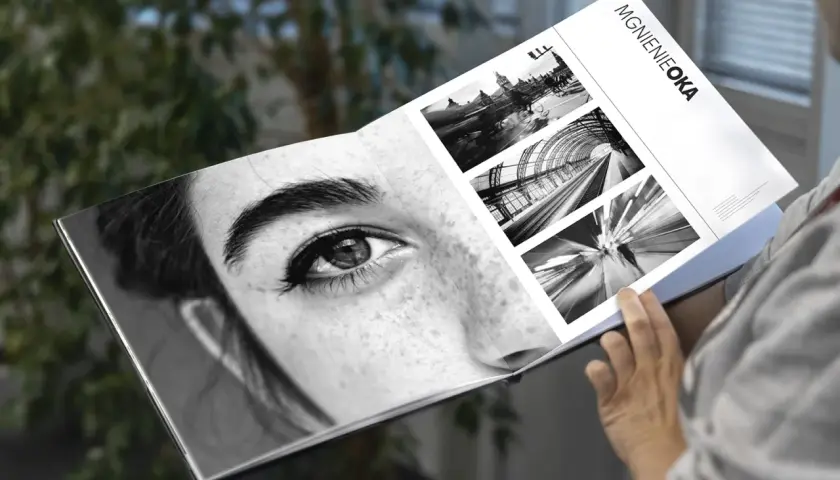 Osoba przegląda album "Mgnienie Oka", gdzie obok zbliżenia oka kobiety znajdują się czarno-białe fotografie miejskich krajobrazów i ruchu.