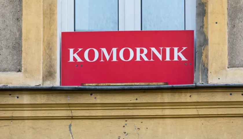 Czerwony szyld z napisem "KOMORNIK" nad oknem. Może oznaczać, że to miejsce, gdzie można dowiedzieć się o kwocie wolnej od zajęcia.