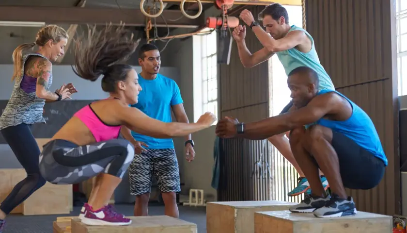 Grupa osób wykonująca ćwiczenia z wyskokami na skrzynie w sali treningowej CrossFit.