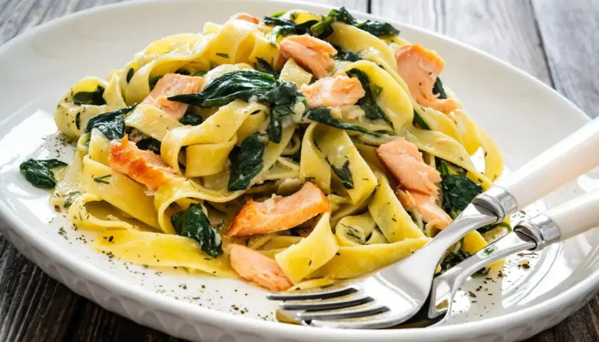 Pappardelle z łososiem i szpinakiem, danie fit, podane na białym talerzu z widelcem i nożem.